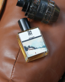 Perfume bottle labeled 'TMH' on a brown leather surface